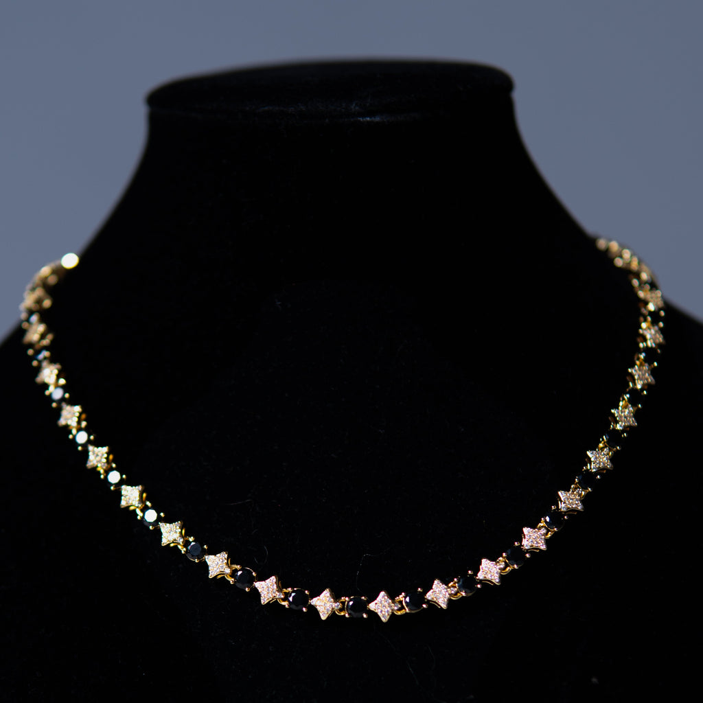 A delicate gold chain necklace featuring small star-shaped charms, displayed on a black velvet jewelry bust against a dark gray background.