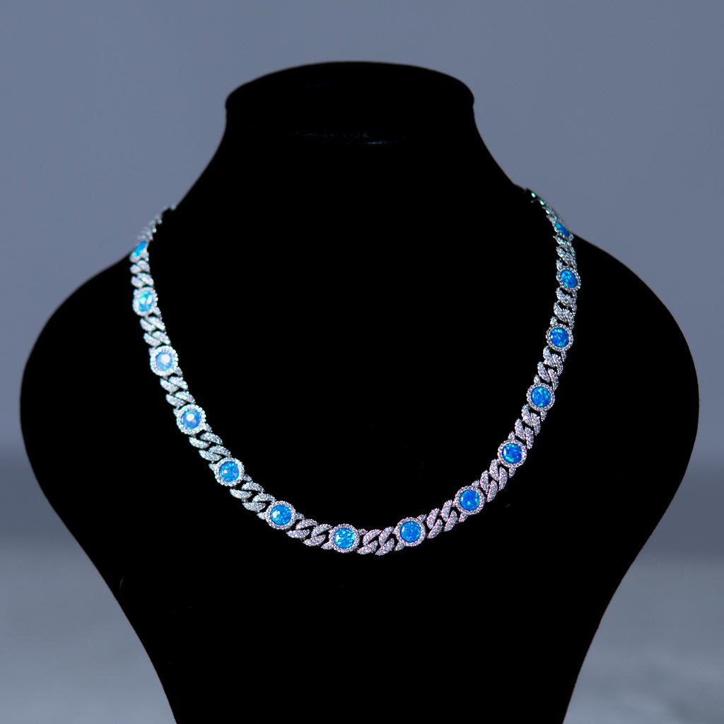 A silver-toned chain necklace with round blue gemstones, displayed on a black jewelry bust against a dark gray background.
