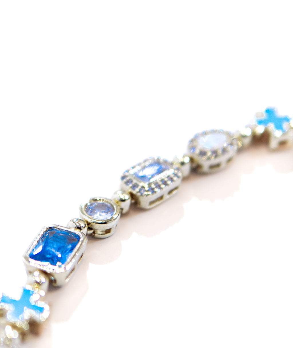 A close-up of a silver-toned bracelet featuring rectangular and round blue gemstones, some surrounded by small clear stones, on a white background.